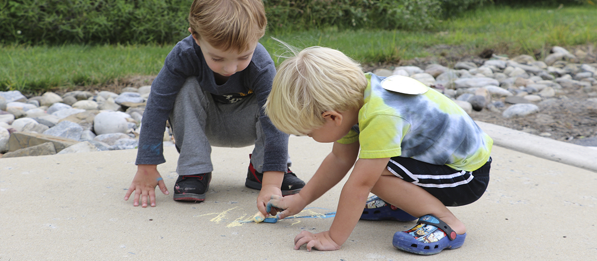 Two children draw with chalk on the sidewalk at the Lab School