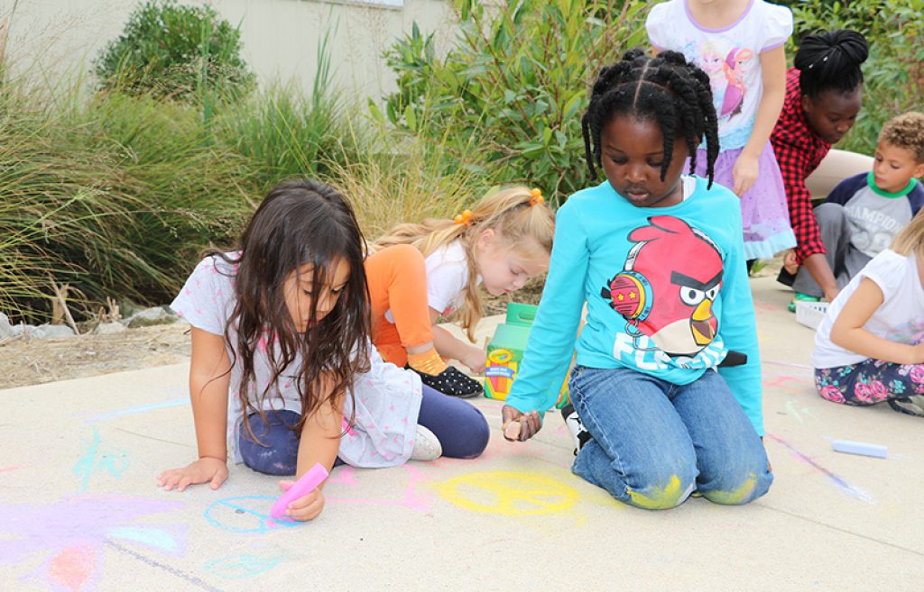 Students draw with chalk on sidewalk outside the UD Lab School