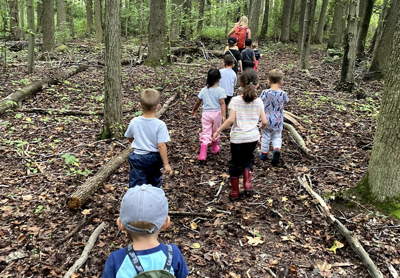 Teacher guides students through the woods outside at the UD Lab School